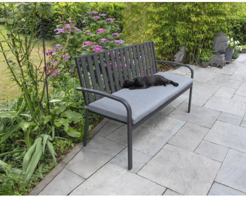 Trädgårdsbänk med grå dyna och liggande katt i trädgården.