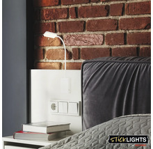 Scen med en vit väggmonterad läslampa ovanför ett nattduksbord med uttag och strömbrytare