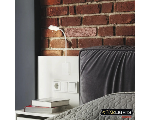 Scen med en vit väggmonterad läslampa ovanför ett nattduksbord med uttag och strömbrytare