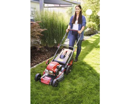 Kvinna skjuter en gräsklippare i trädgården.