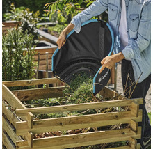 En person tömmer en Gardena-lövsäck i en träkolsbehållare i trädgården.