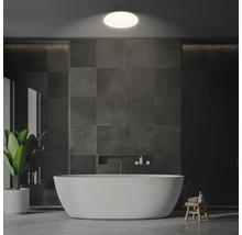 Modernt badrum med fristående badkar, gråa kakelplattor och krukväxt