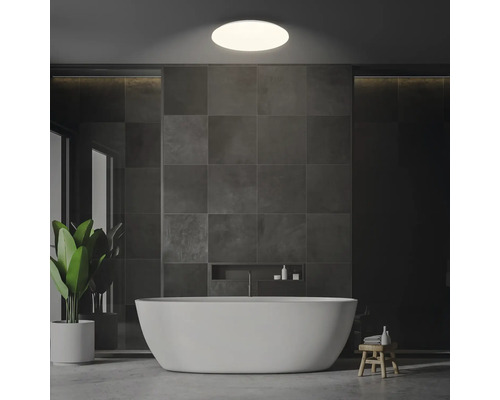 Badrum med fristående badkar, gråa kakelplattor och taklampa