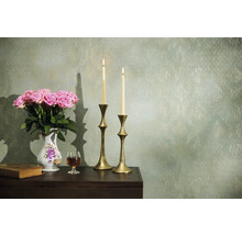 Dekorativt arrangemang med rosor, ljus och antika element på ett bord framför en mönstrad vägg