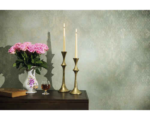 Dekorativt arrangemang med rosor, ljus och antika element på ett bord framför en mönstrad vägg