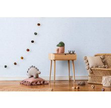 Ljust barnrum med trägolv, träbord, rottingfåtölj och dekorativa element som girlang, kuddar och en växt.