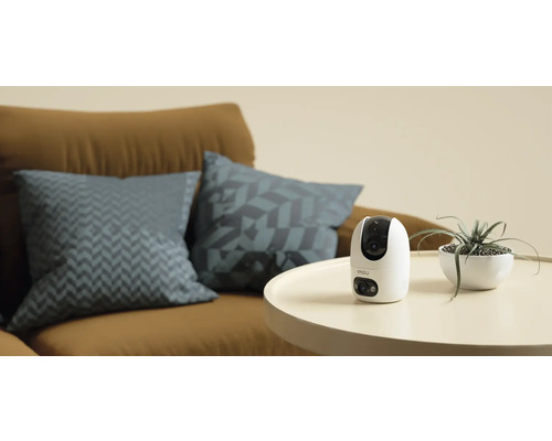 Imou övervakningskamera på ett bord bredvid en krukväxt och en soffa
