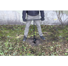 En person använder ett jordborr för att borra ett hål i marken.