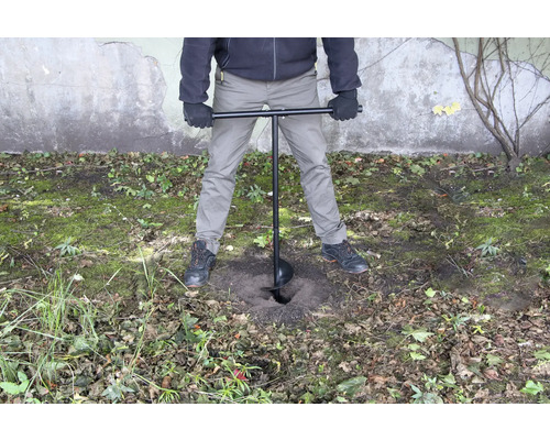 En person använder ett jordborr för att borra ett hål i marken.