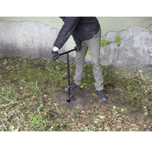 En person borrar ett hål i marken med ett jordborr.