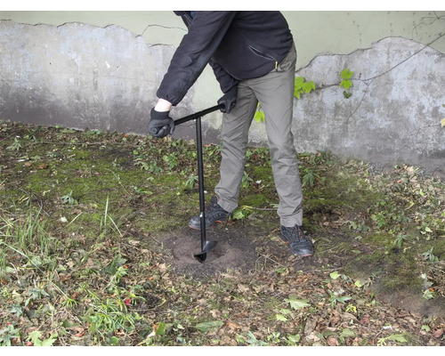 En person borrar ett hål i marken med ett jordborr.