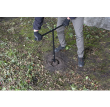 En person använder ett jordborr för att borra ett hål i marken.