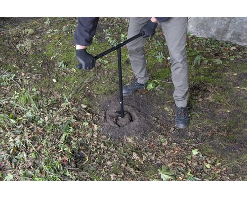 En person använder ett jordborr för att borra ett hål i marken.