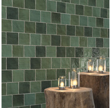 Vägg med kvadratiska, gröna plattor och lyktor på trädstubbar