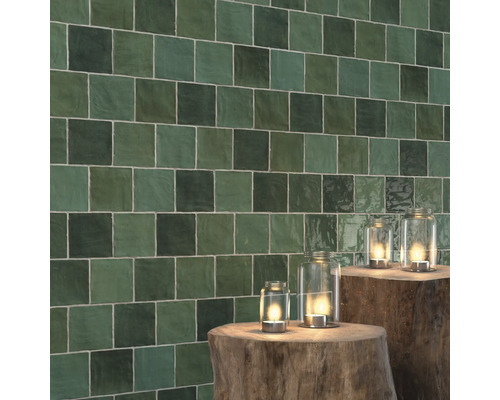 Vägg med kvadratiska, gröna plattor och lyktor på trädstubbar