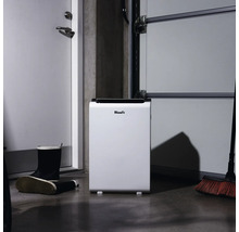 Vit Woods luftavfuktare i ett garage bredvid ett par gummistövlar och en kvast.