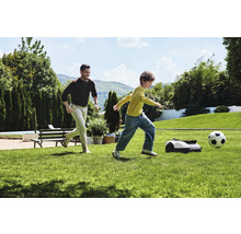 Man och barn spelar fotboll med robotgräsklippare i trädgården.