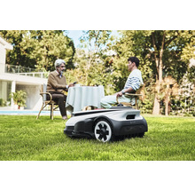 Scen med en robotgräsklippare i trädgården medan två personer sitter vid ett bord