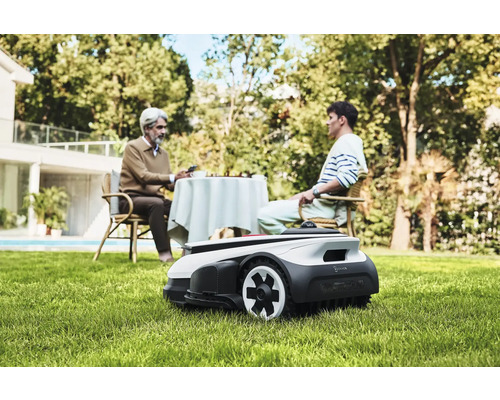 Scen med en robotgräsklippare i trädgården medan två personer sitter vid ett bord