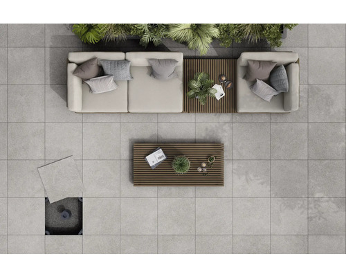 Översikt över en terrass med ljusgrå terrassplattor, loungemöbler och träbord