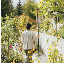 Kvinna i trädgården med kratta och kultivator bland blomsterrabatterna