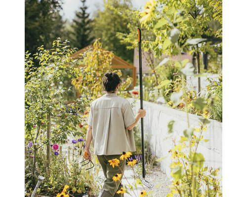 Kvinna i trädgården med kratta och kultivator bland blomsterrabatterna