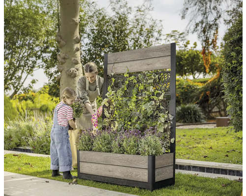 Kvinna och barn planterar en planteringslåda med spaljé i trädgården.