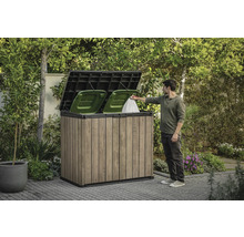 Soptunneskåp i trä med två gröna soptunnor och en person som kastar en soppåse i den