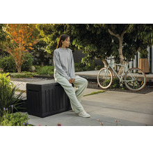 Trädgårdsscen med en sittande person på en förvaringslåda och en cykel i bakgrunden