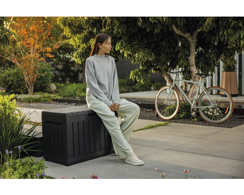 Trädgårdsscen med en sittande person på en förvaringslåda och en cykel i bakgrunden