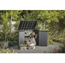 Trädgårdsscen med öppet redskapsskåp där en kvinna förvarar trädgårdsredskap.