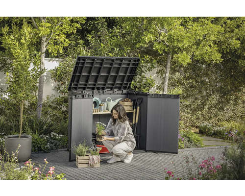 Trädgårdsscen med öppet redskapsskåp där en kvinna förvarar trädgårdsredskap.