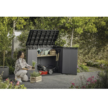 En kvinna planterar blommor framför ett öppet trädgårdsskåp med trädgårdsredskap