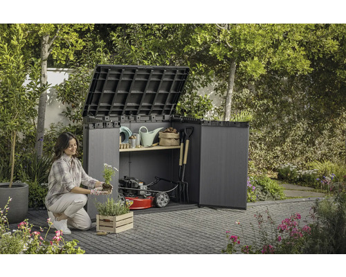 En kvinna planterar blommor framför ett öppet trädgårdsskåp med trädgårdsredskap