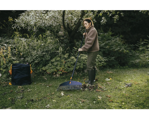 Kvinna krattar löv i trädgården med en lövgrep och en trädgårdssäck.