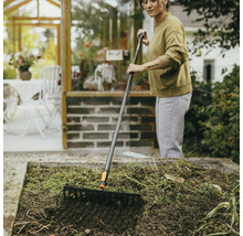 Kvinna krattar trädgårdsland med en trädgårdskratta