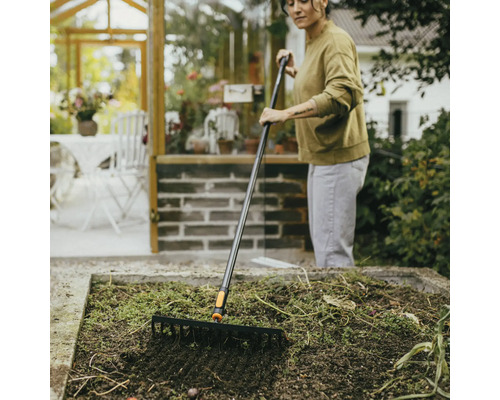 Kvinna krattar trädgårdsland med en trädgårdskratta