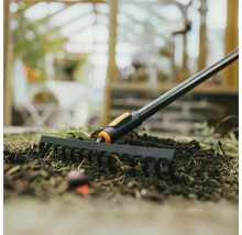 Trädgårdsräfsa i bruk på en bädd med jord.