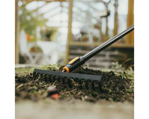 Trädgårdsräfsa i bruk på en bädd med jord.