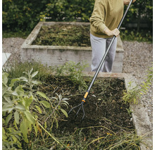 En person arbetar med en trädgårdskultivator i en upphöjd trädgård.