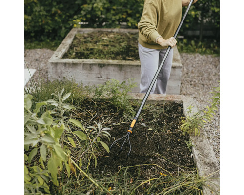 En person arbetar med en trädgårdskultivator i en upphöjd trädgård.