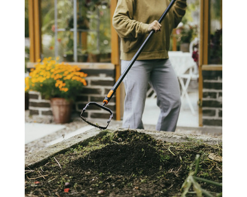 Person som tar bort ogräs med en oscilloskopisk hacka i en trädgårdsbädd.