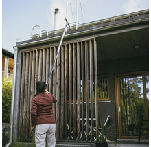 En person rengör en takränna med en takrännsrengörare framför ett hus.