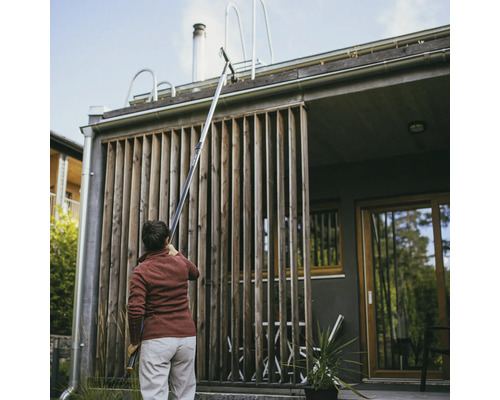 En person rengör en takränna med en takrännsrengörare framför ett hus.