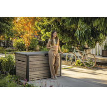 Trädgårdsscen med en kvinna som lutar sig mot en förvaringslåda i trä och håller en kaffekopp.