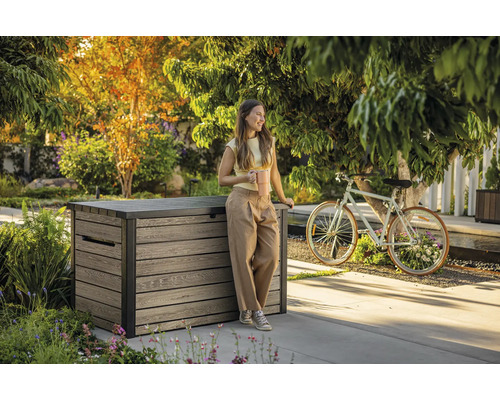 Trädgårdsscen med en kvinna som lutar sig mot en förvaringslåda i trä och håller en kaffekopp.