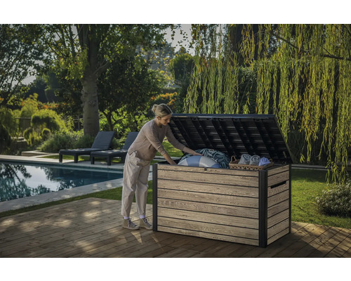 En kvinna öppnar en trädgårdskista på en träterrass bredvid en pool och trädgård.