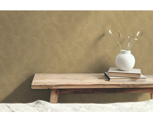 Dekorativ tapet med cirkelmönster på väggen ovanför en träbänk med böcker och en vas.