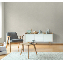 Vardagsrum med fåtölj, bord och byrå framför en strukturerad tapet