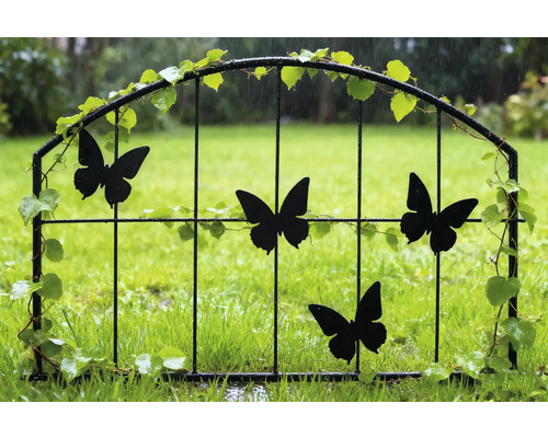 Dekorativ trädgårdsgrind med fjärilsmotiv och växtdekorationer i trädgården.